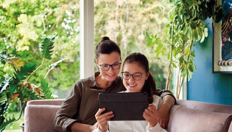 Eine Frau und ihre Tochter sitzen auf dem Sofa und sehen in ein Tablet